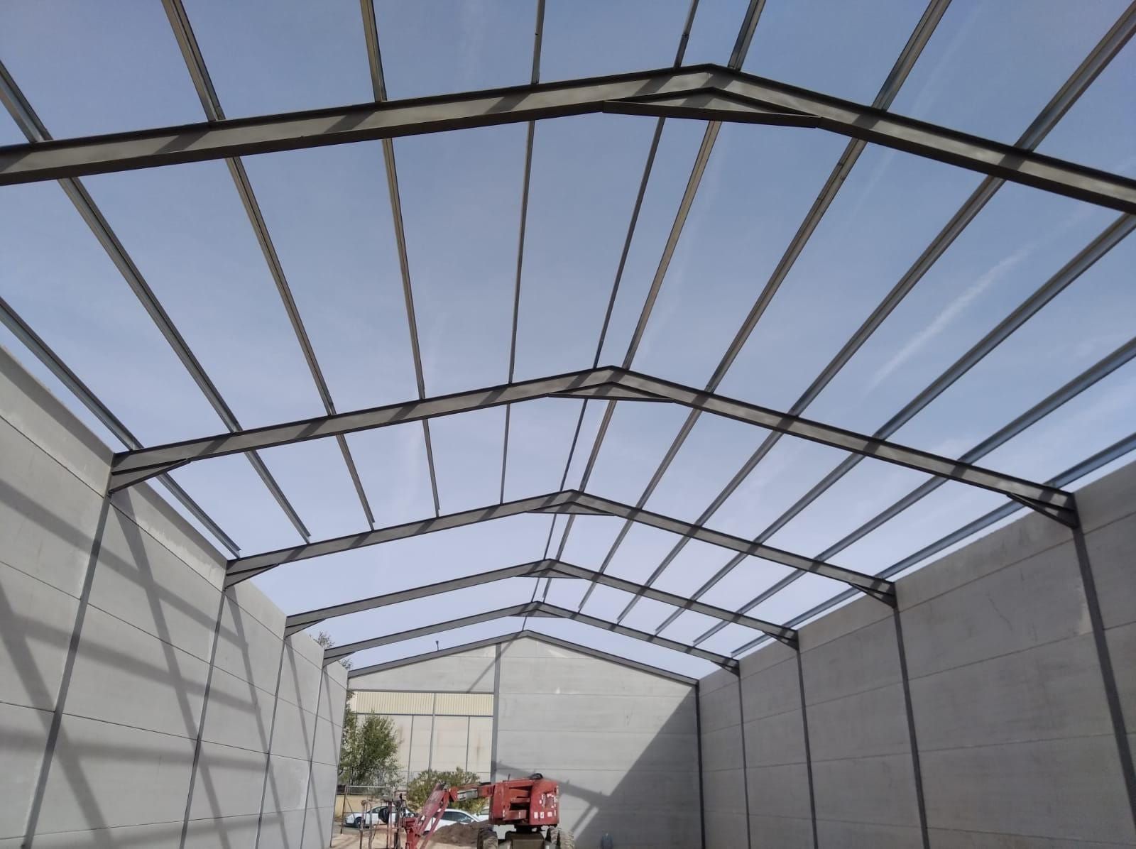 Vista interior de un edificio con estructura de techo de metal y paredes de hormigón, a lo lejos se ve un camión.