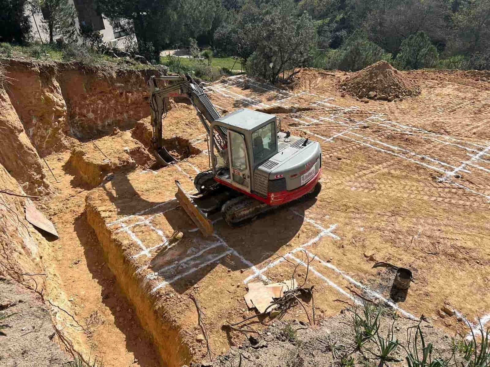Excavadora en un pozo de tierra; líneas blancas marcan un sitio de construcción.