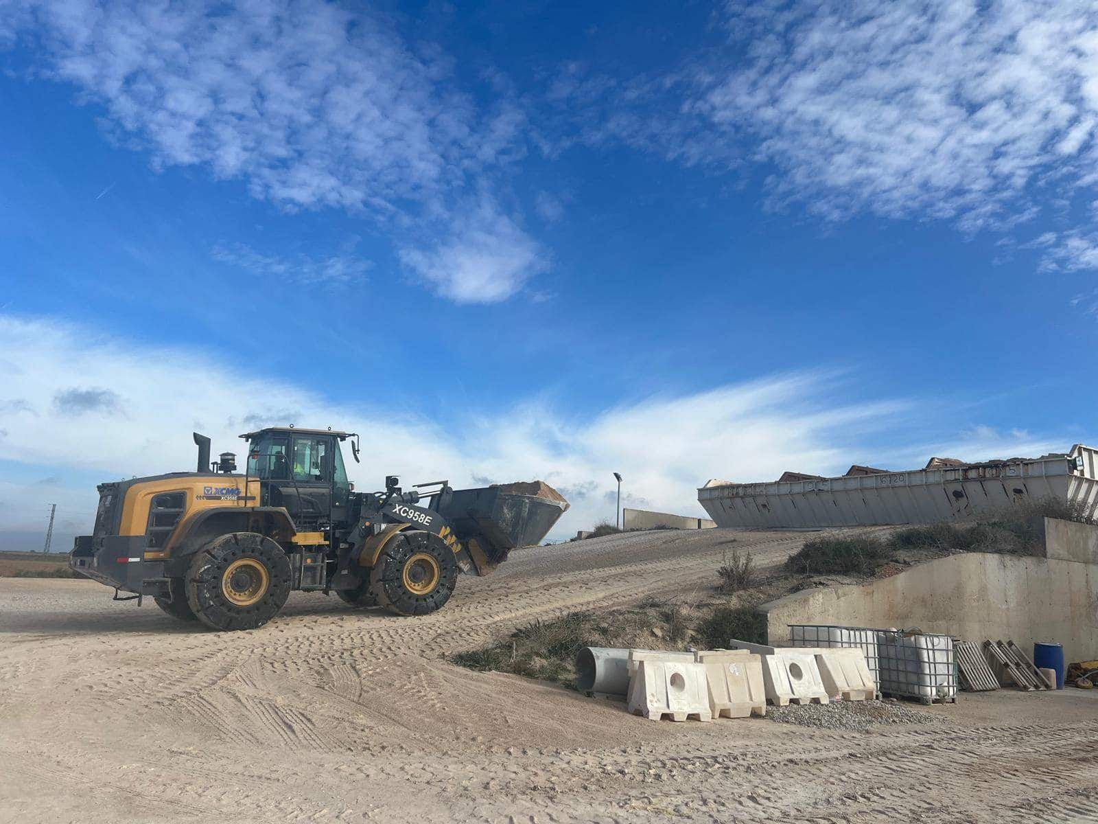 Un cargador frontal amarillo está trabajando en un terreno arenoso bajo un cielo azul.