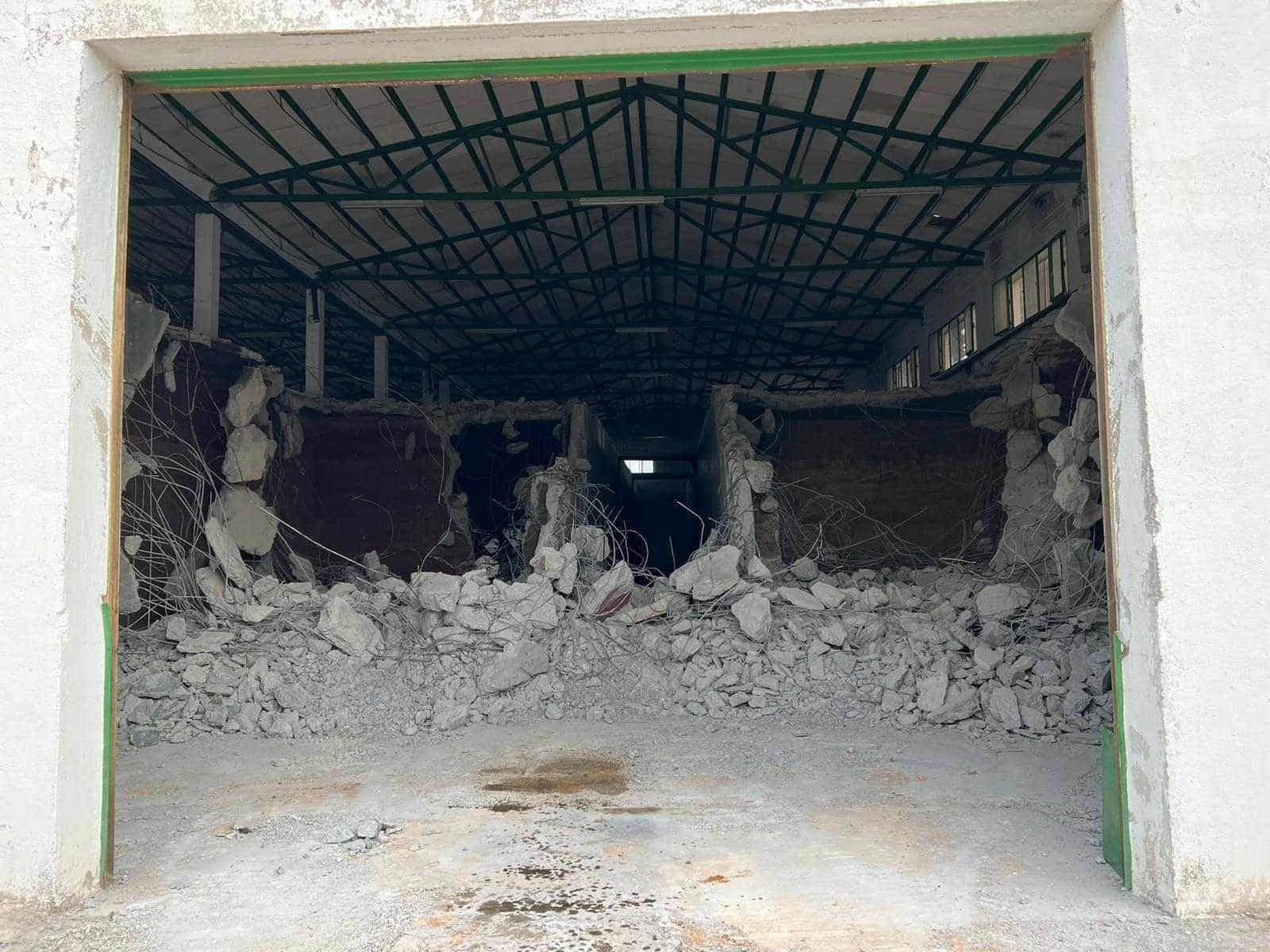 Interior de un edificio demolido, con escombros al frente y una puerta con detalles verdes.