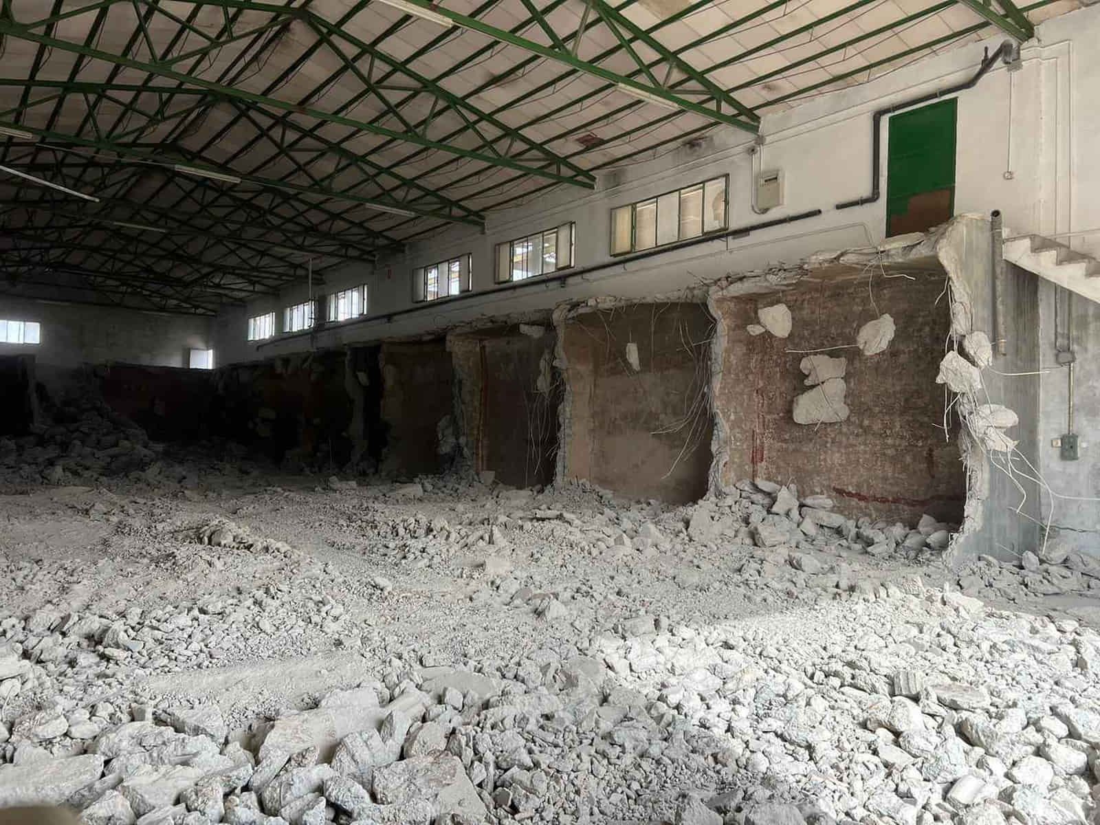 Interior de un almacén demolido con montones de escombros en el suelo y paredes expuestas.