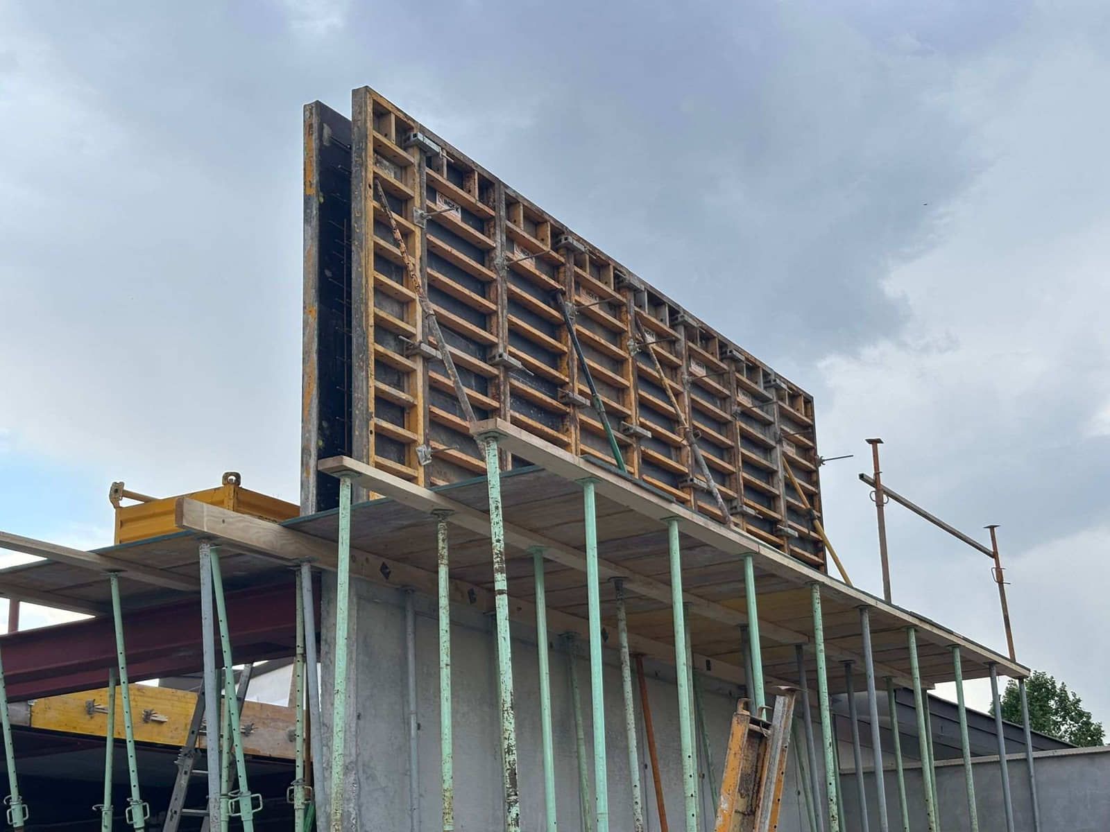 Muro de hormigón en construcción con andamios y encofrados frente a un cielo nublado.