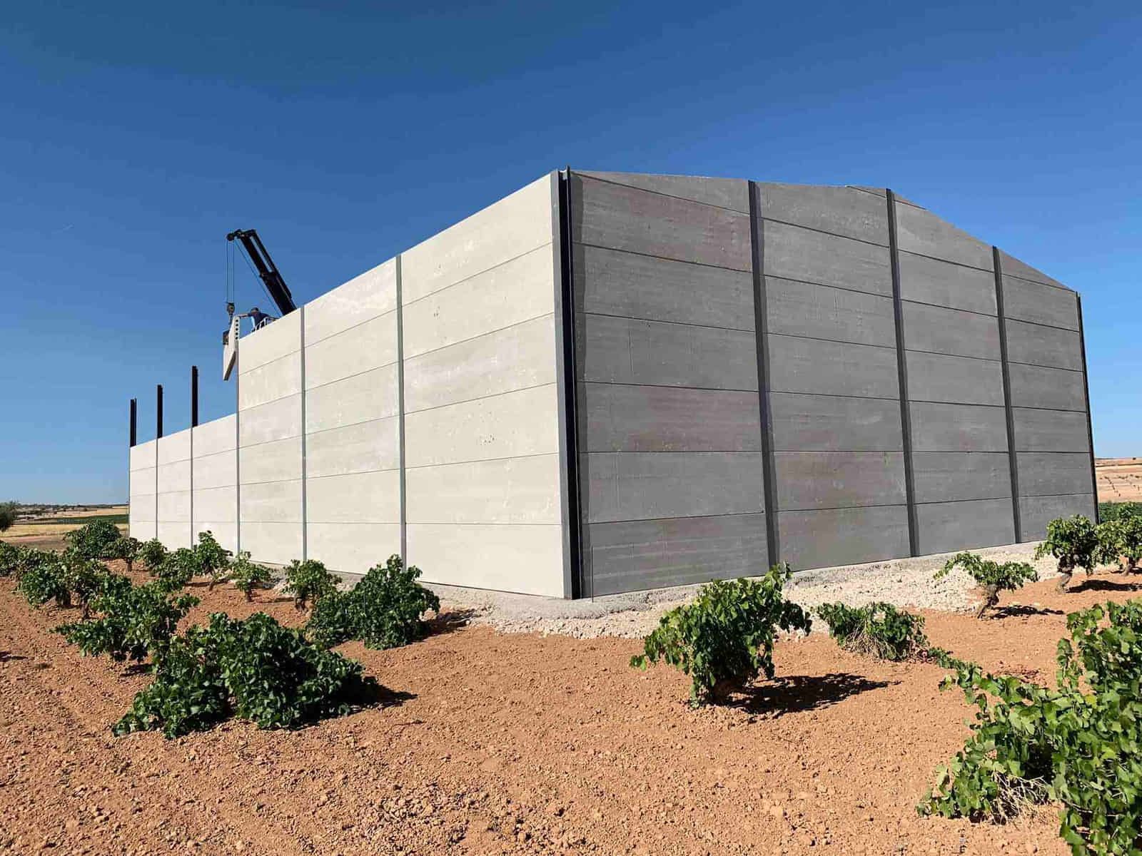 Gran edificio de hormigón gris en un viñedo bajo un cielo azul.