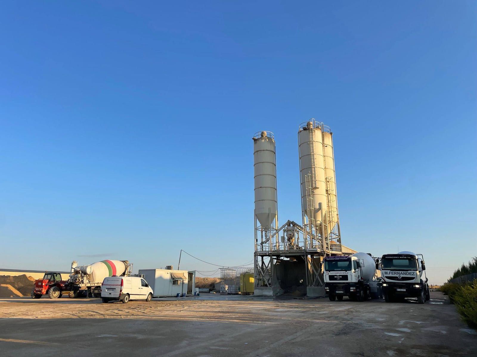 Planta mezcladora de hormigón con camiones bajo un cielo azul claro.