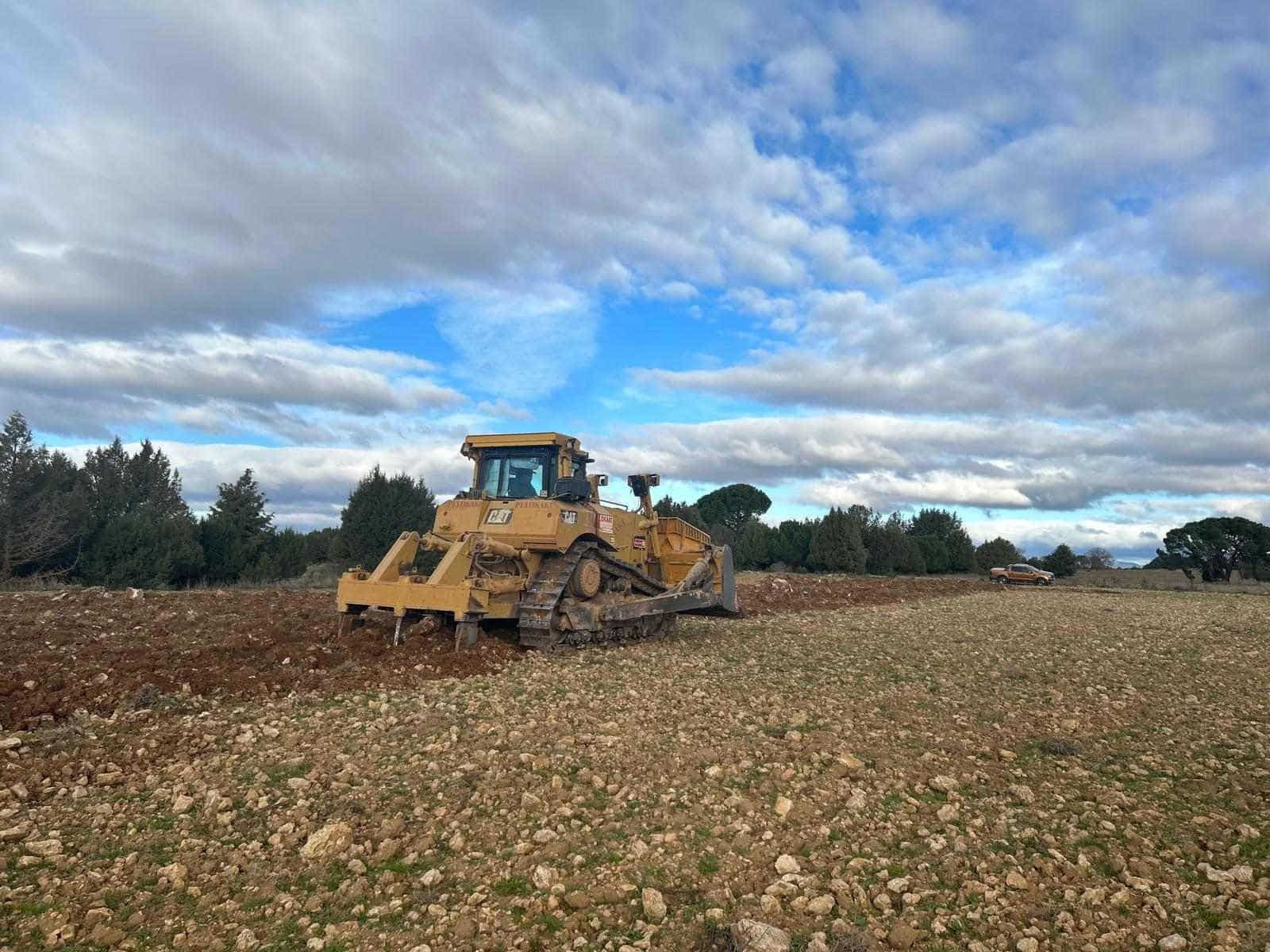 Una excavadora amarilla arando un campo bajo un cielo azul nublado.