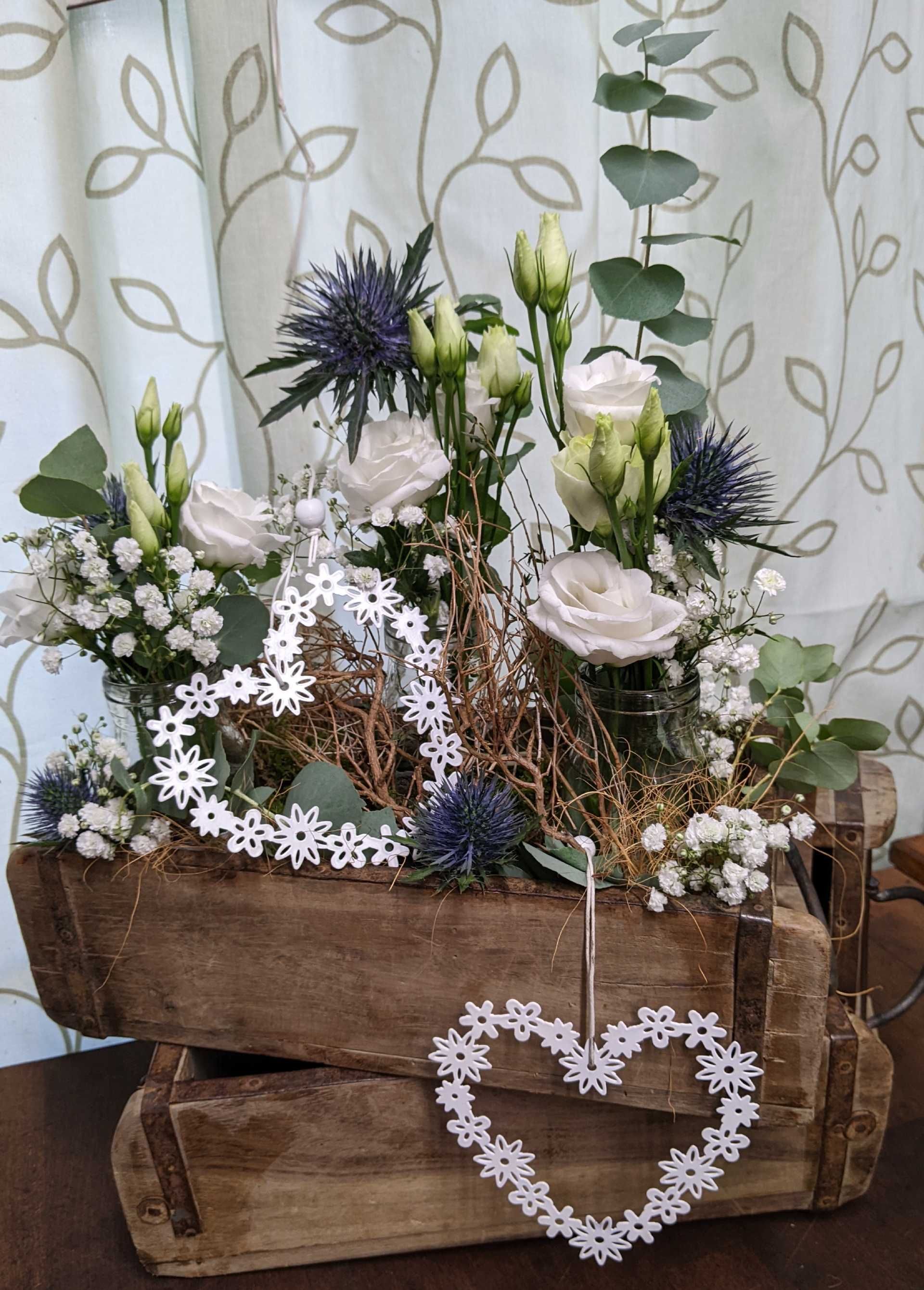 Eine dekorative Holzkiste, die mit verschiedenen Blumenarrangements gefüllt ist mit herzförmiger Dekoration.