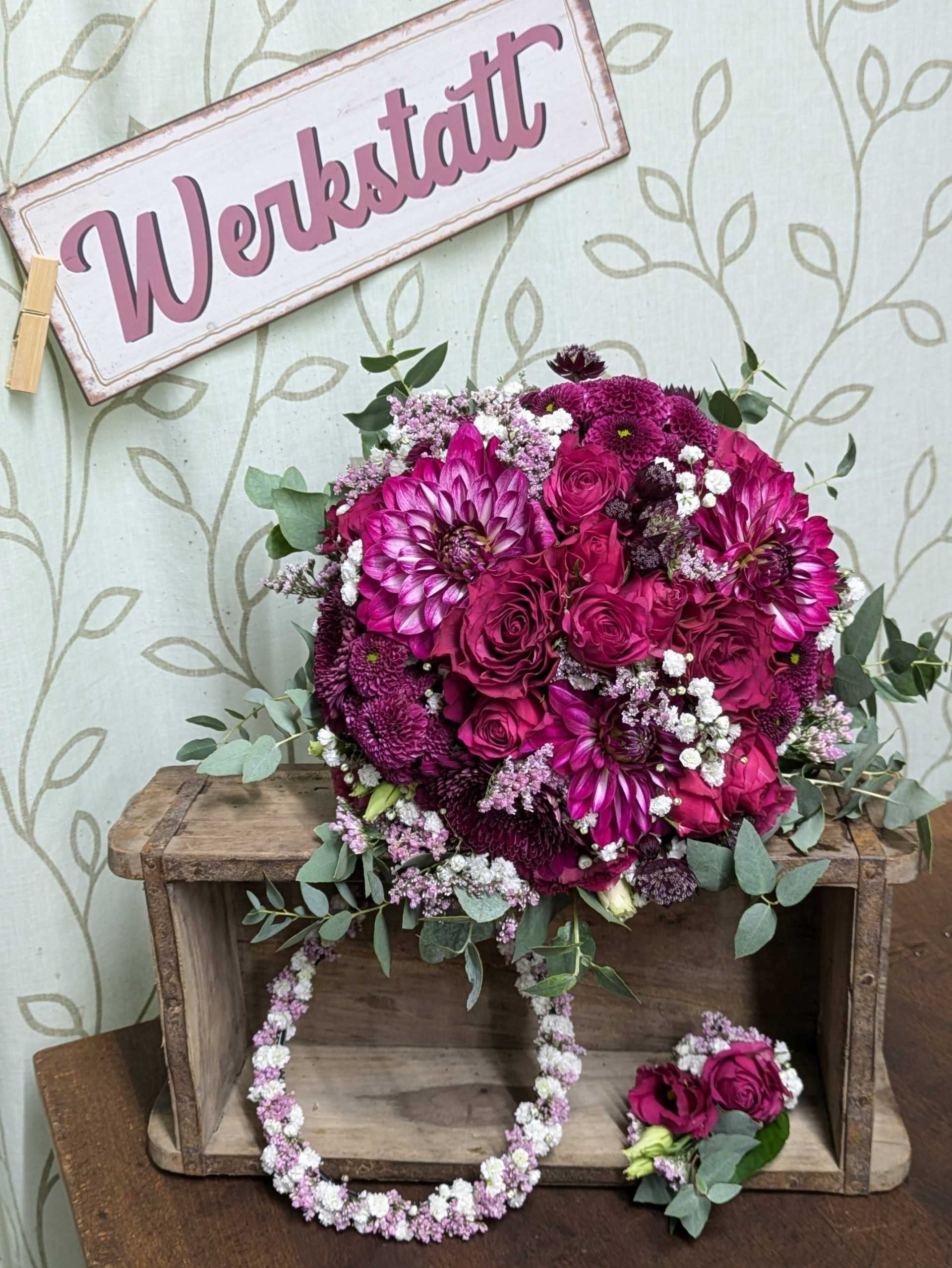 Ein Strauß aus lila Blumen und Grünzeug wird auf einer Holzkiste präsentiert.