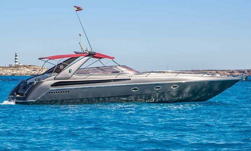 Yate a motor gris en aguas azules con toldo rojo. Faro al fondo.