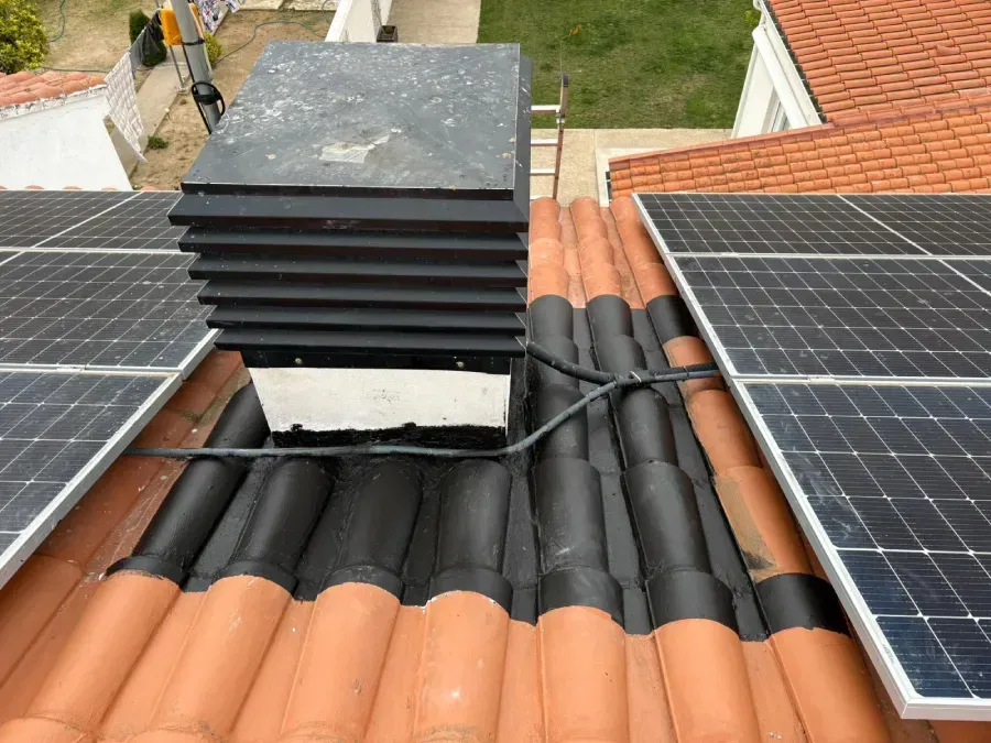 Una chimenea negra sobre un tejado de tejas flanqueada por hileras de paneles 