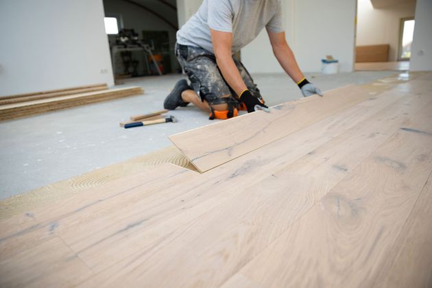 Eine Person verlegt helle Holzdielen in einem im Bau befindlichen Raum.
