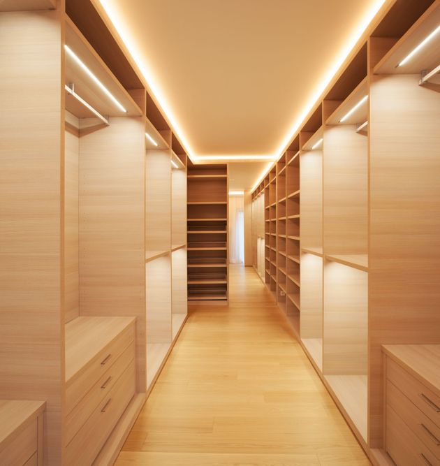 Ein minimalistischer, gut beleuchteter begehbarer Kleiderschrank mit hellen Holzregalen, Schubladen und integrierter LED-Streifenbeleuchtung.