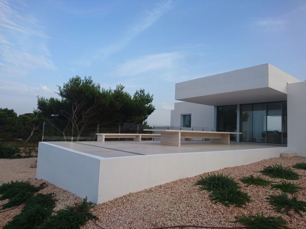 Casa moderna blanca con zona de estar al aire libre, grava color canela y cielo azul.