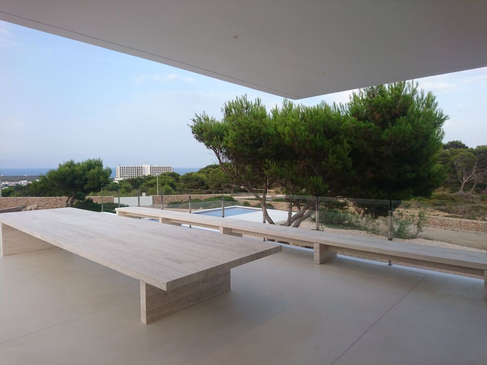 Patio exterior con mesa larga y bancos, con vistas a un paisaje con árboles y piscina.