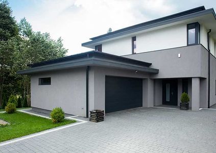 Casa moderna de dos pisos con fachada gris, garaje adjunto y entrada pavimentada.
