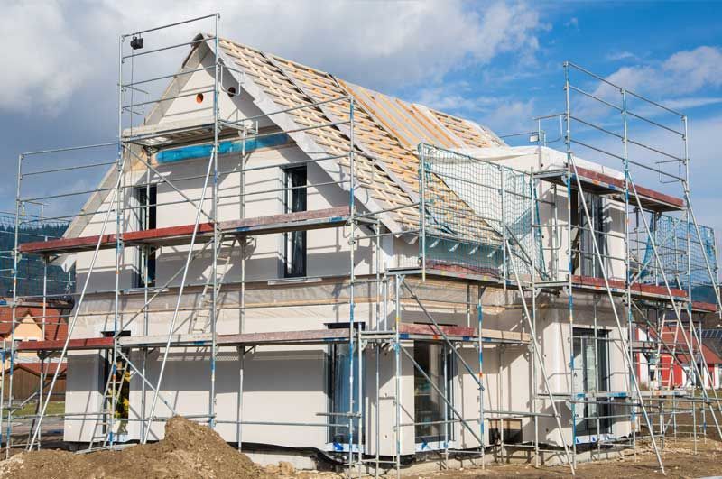 Casa en construcción con andamios y techo a la vista en un barrio.