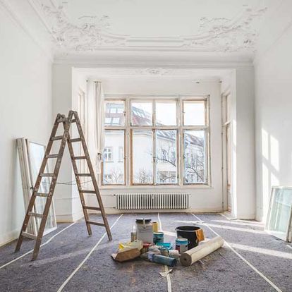 Habitación con materiales de pintura, escalera y ventana, lo que sugiere renovación.