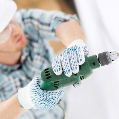 Persona que usa gafas de seguridad y guantes utilizando un taladro verde.