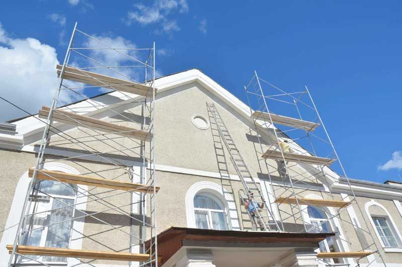 Exterior de un edificio con andamios y escalera. Hombre en la escalera. Cielo azul.