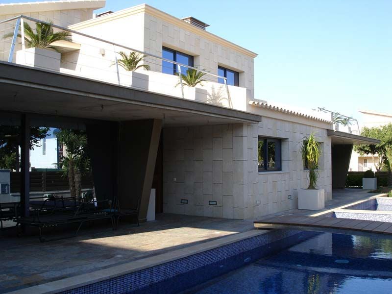 Casa moderna beige con piscina. Palmeras, cielo azul y un puente de madera.