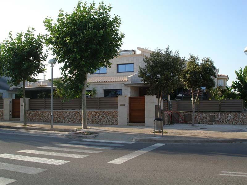 Casa con fachada de piedra, valla de madera y arboles, cerca de paso de peatones.