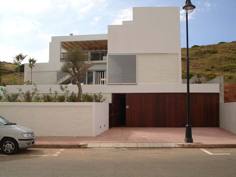 Casa moderna de color blanco y madera con garaje y una colina al fondo.