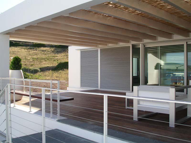 Moderna terraza con suelo de madera, barandillas blancas y techo sombreado con vistas a una colina cubierta de hierba.
