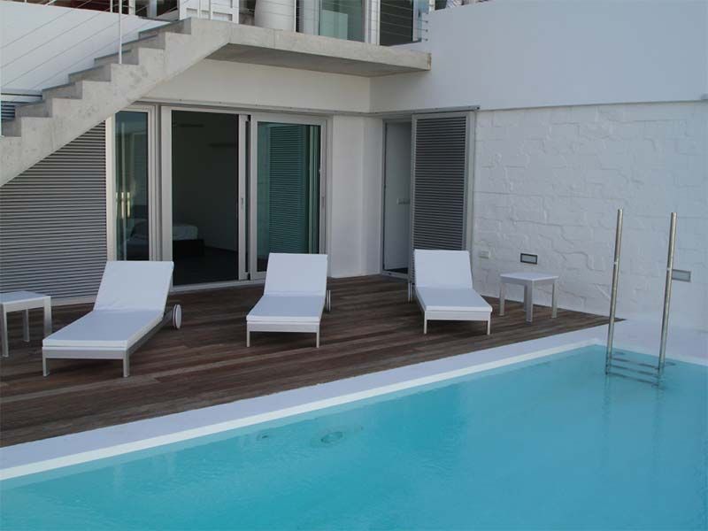 Junto a la piscina con tres tumbonas blancas en una terraza de madera al lado de una piscina, un edificio blanco y escaleras.