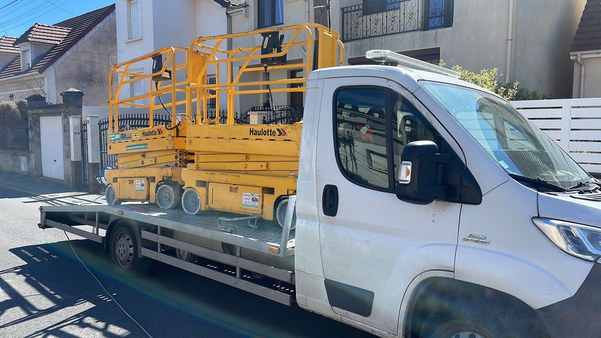 Un pont élévateur utilitaire jaune monté sur une camionnette blanche garée dans une rue résidentielle