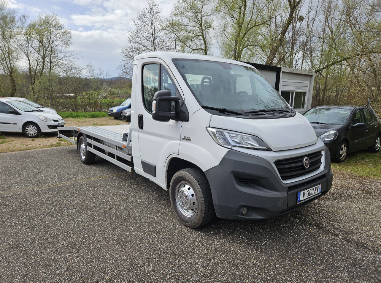 Camion-plateau blanc stationné sur un terrain gravillonné avec des arbres et d'autres voitures en arrière-plan