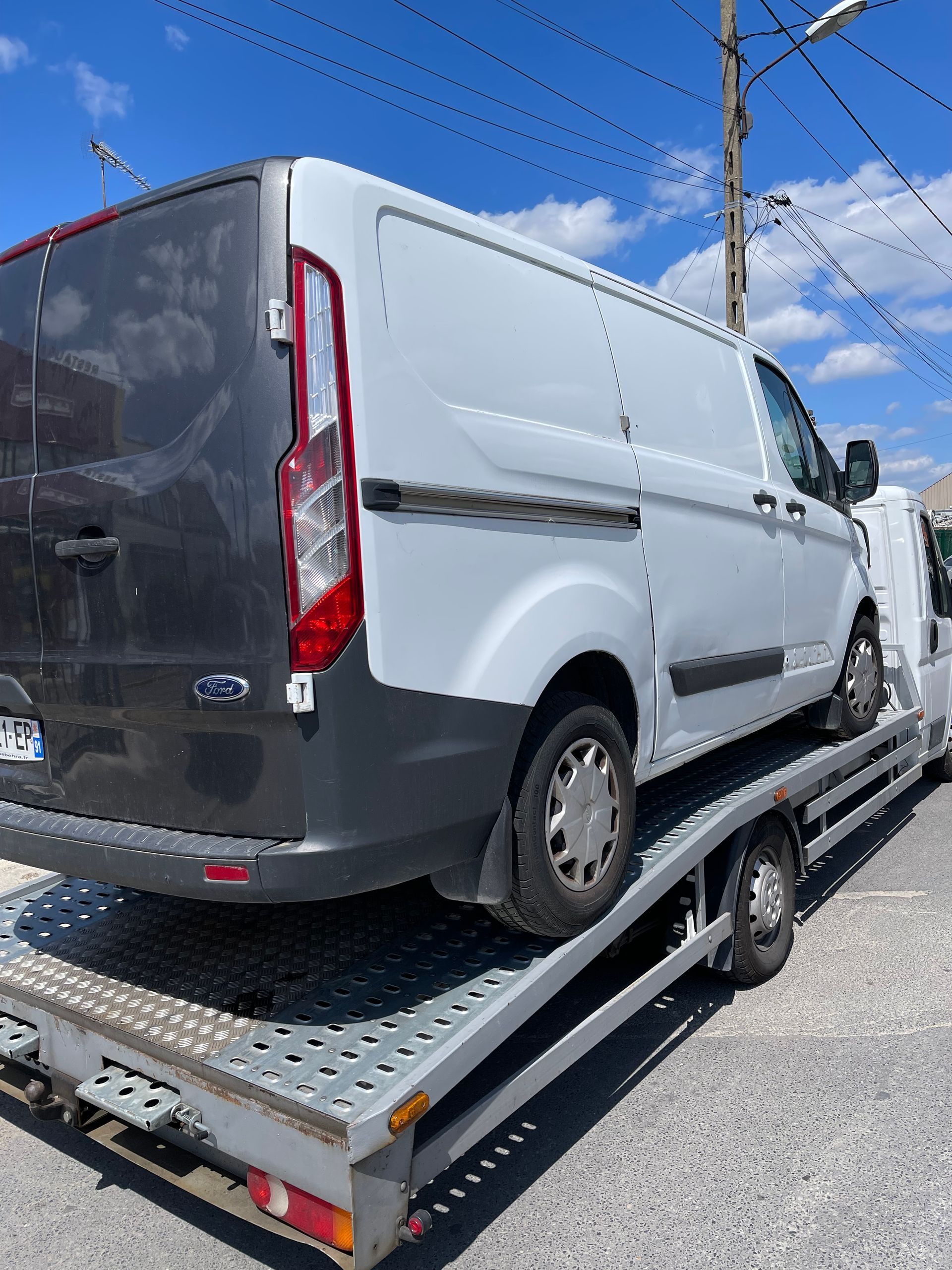Fourgonnette blanche sur une dépanneuse à plateau sous un ciel bleu