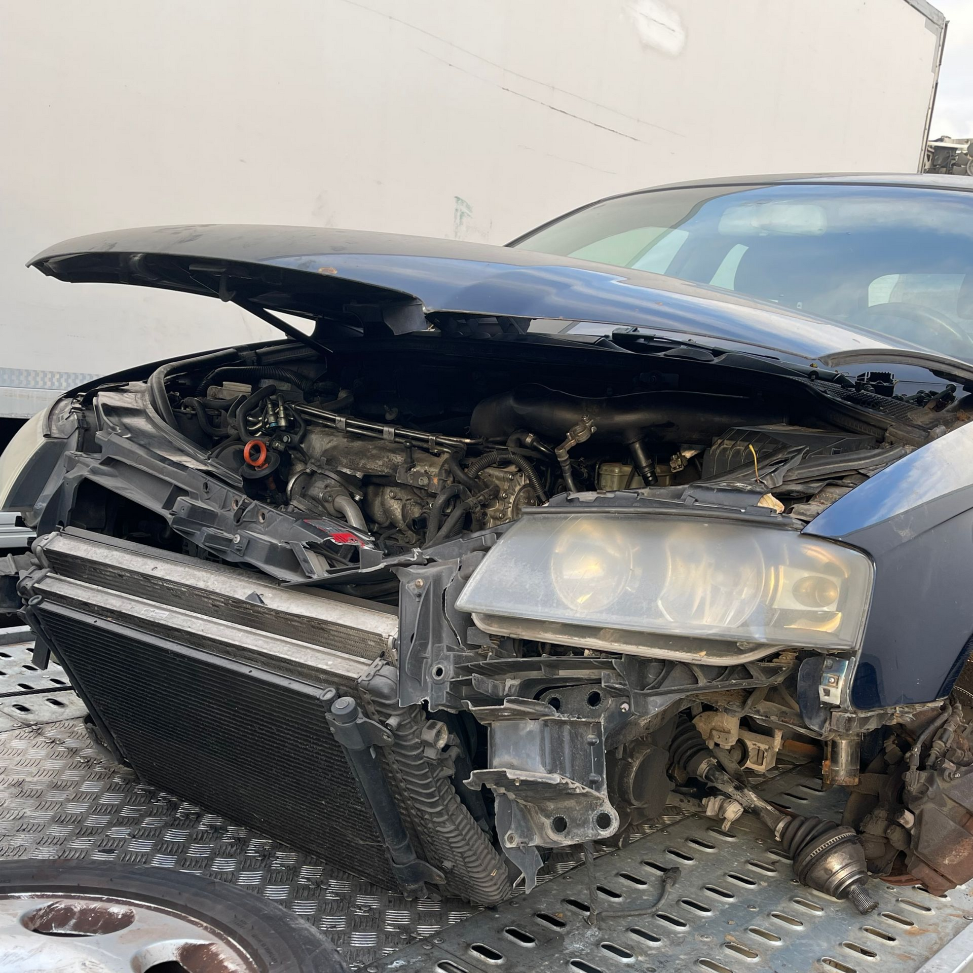 Vue de face d'une voiture noire endommagée, avec un capot froissé et des parties du moteur apparentes