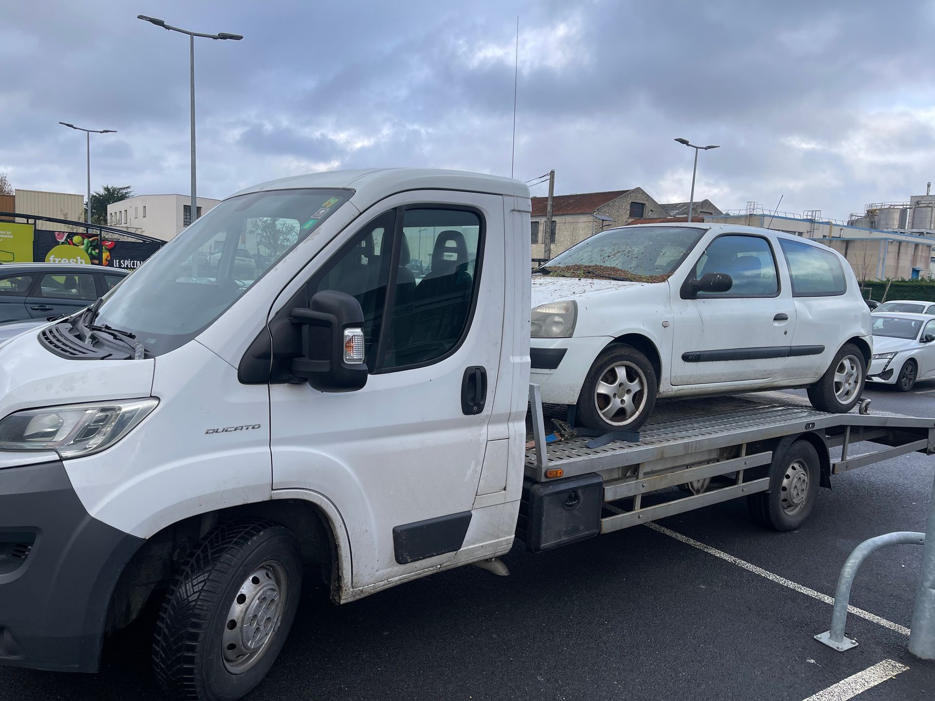 Une dépanneuse blanche transportant une voiture blanche sur un plateau dans un parking