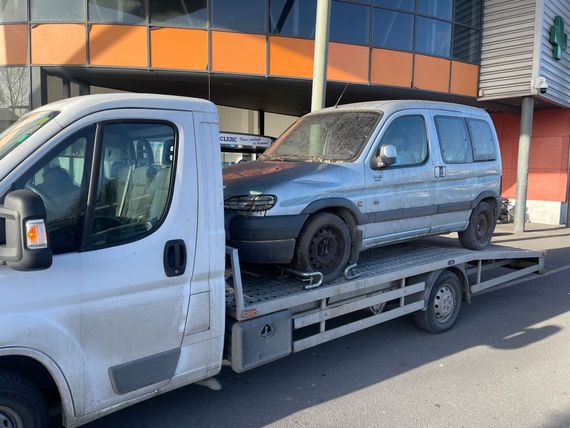 Une camionnette grise chargée sur une dépanneuse à plateau devant un bâtiment aux fenêtres orange et bleues