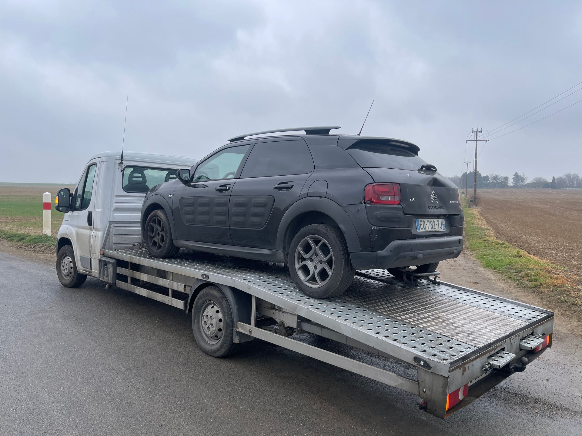 Un SUV foncé chargé sur une dépanneuse à plateau sur une route de campagne par temps couvert