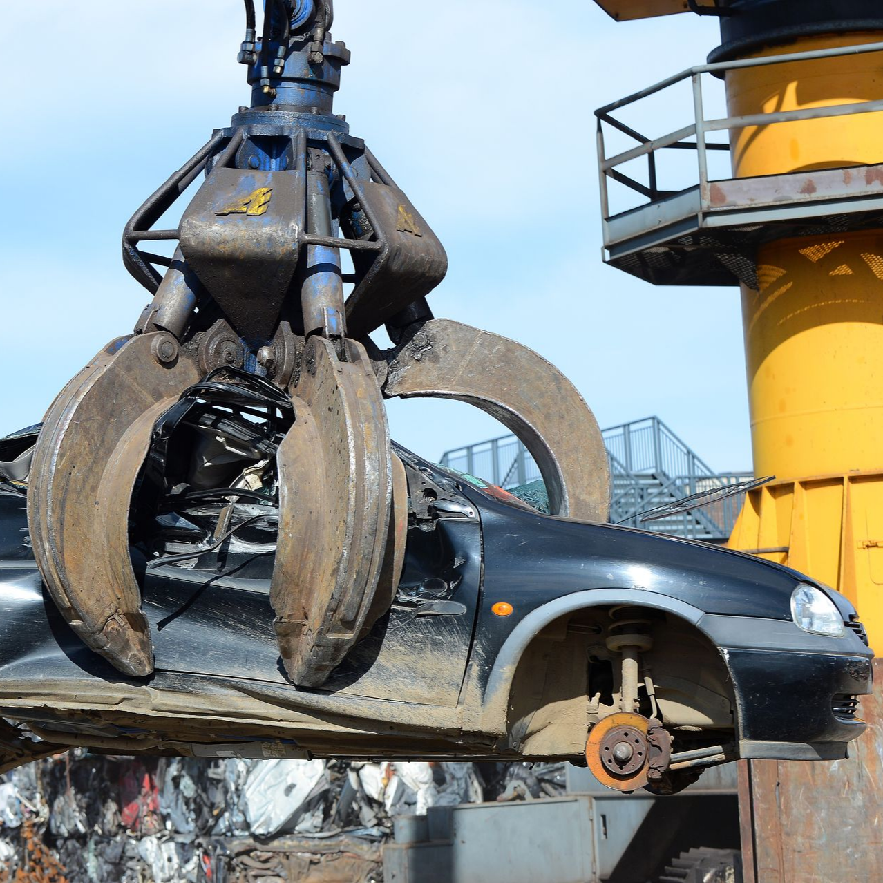 Une pince hydraulique agrippe une voiture noire écrasée dans une casse