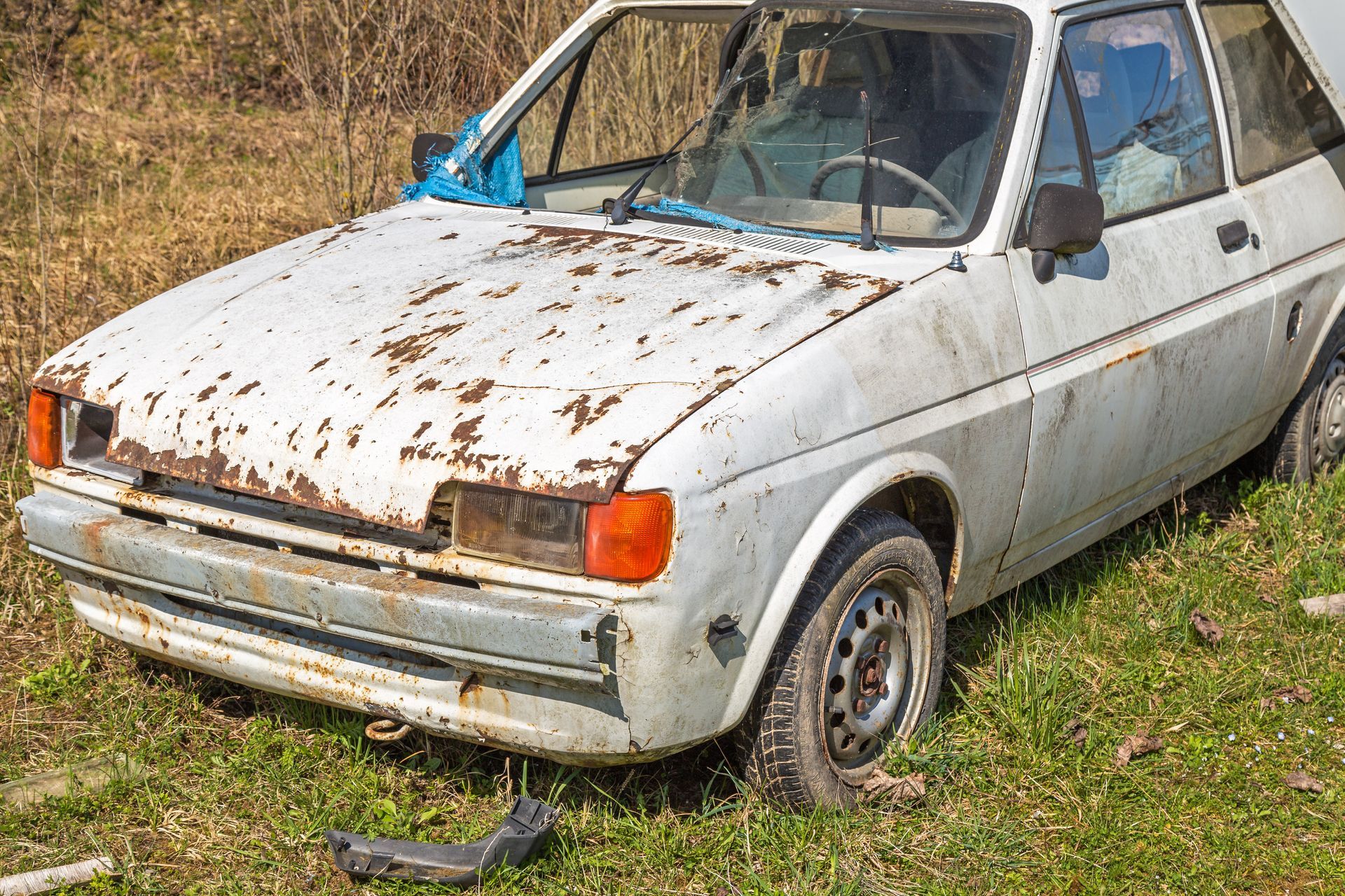 Voiture compacte blanche rouillée garée sur l'herbe, l'avant endommagé et du ruban adhésif bleu sur le pare-brise