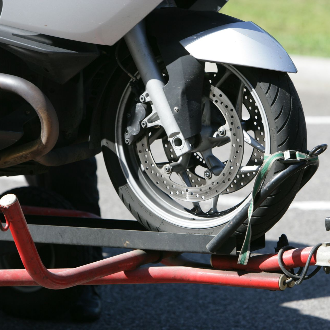 Roue avant d'une moto fixée sur une remorque à l'aide d'une cale rouge et d'une sangle