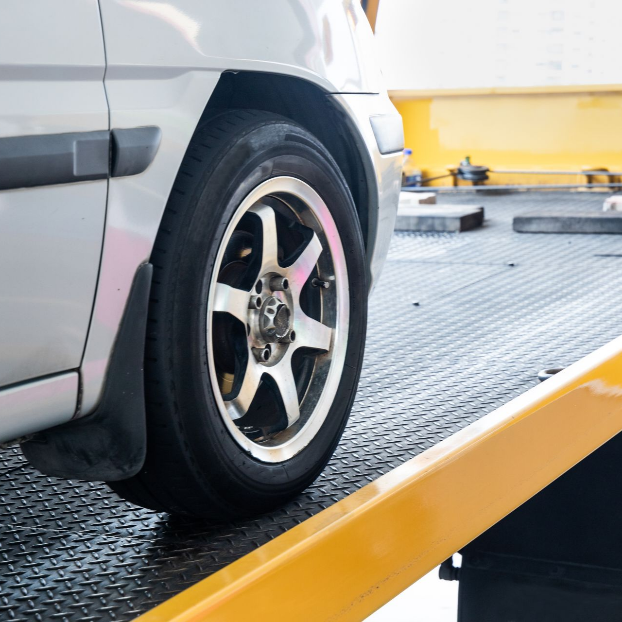 Voiture argentée sur une rampe de dépanneuse jaune, la roue avant reposant sur une plateforme métallique noire