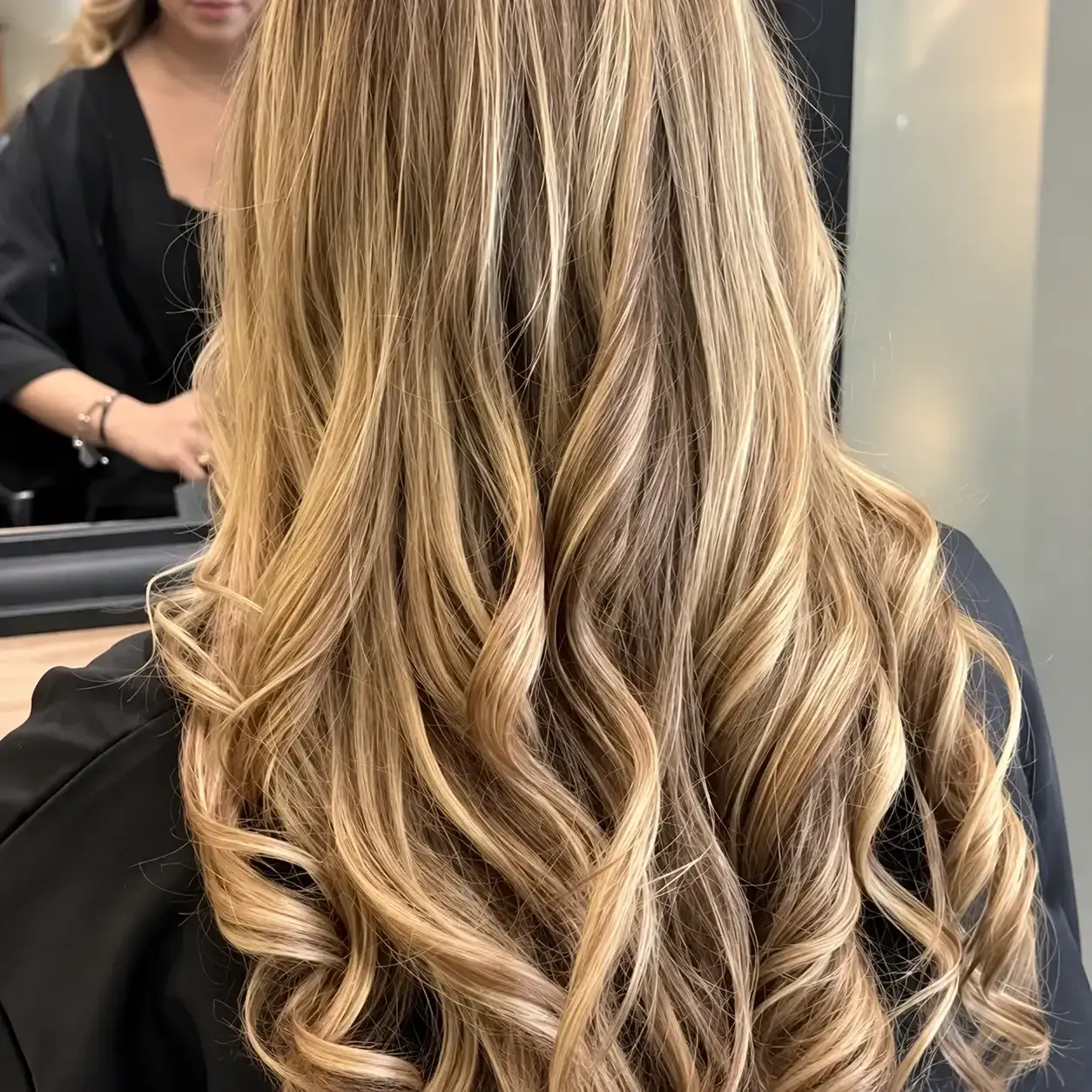 Cabello largo rubio ondulado con reflejos, peinado en rizos sueltos en un salón de belleza.