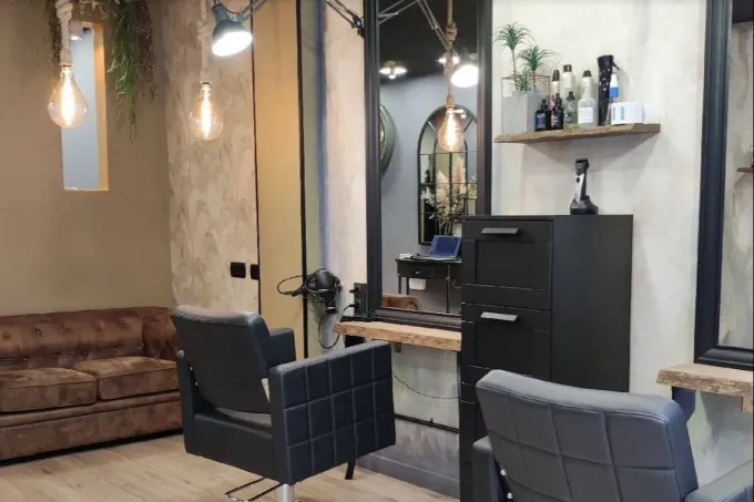 Salón moderno con sillones de peluquería negros, espejo y sofá marrón en un interior minimalista.