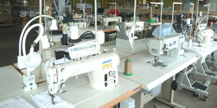 Des rangées de machines à coudre sur des tables blanches, dans un environnement d'usine.