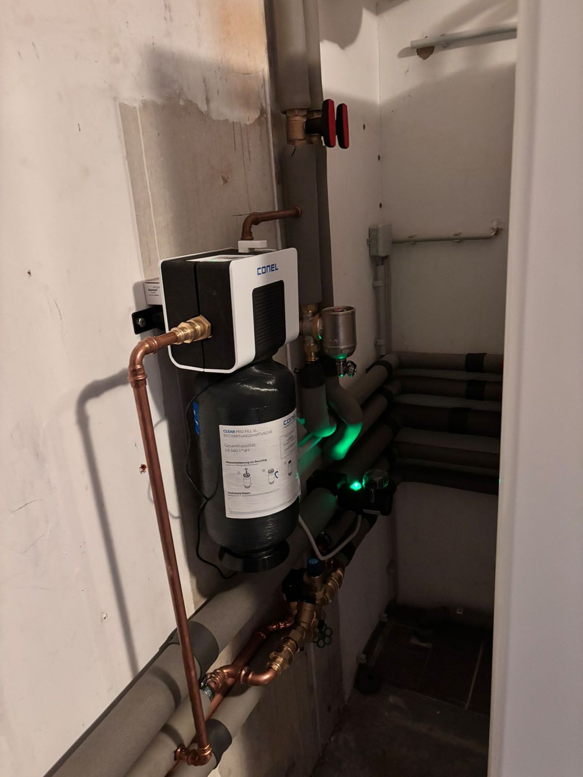 Wasserfiltersystem mit Kupferrohren, montiert an einer weißen Wand in einem Hauswirtschaftsraum.