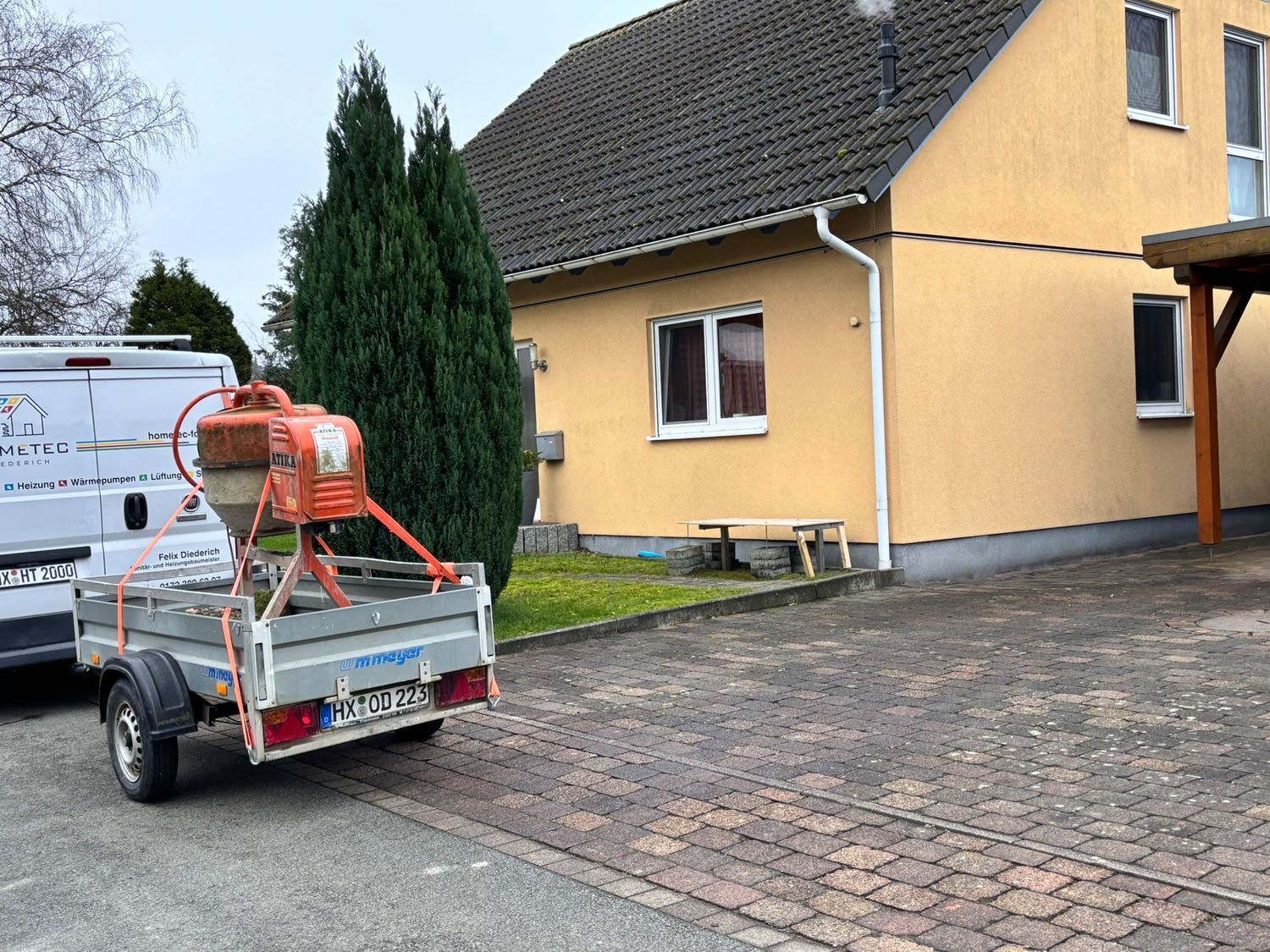 Anhänger mit Betonmischer vor einem gelben Haus geparkt, daneben ein Lieferwagen.