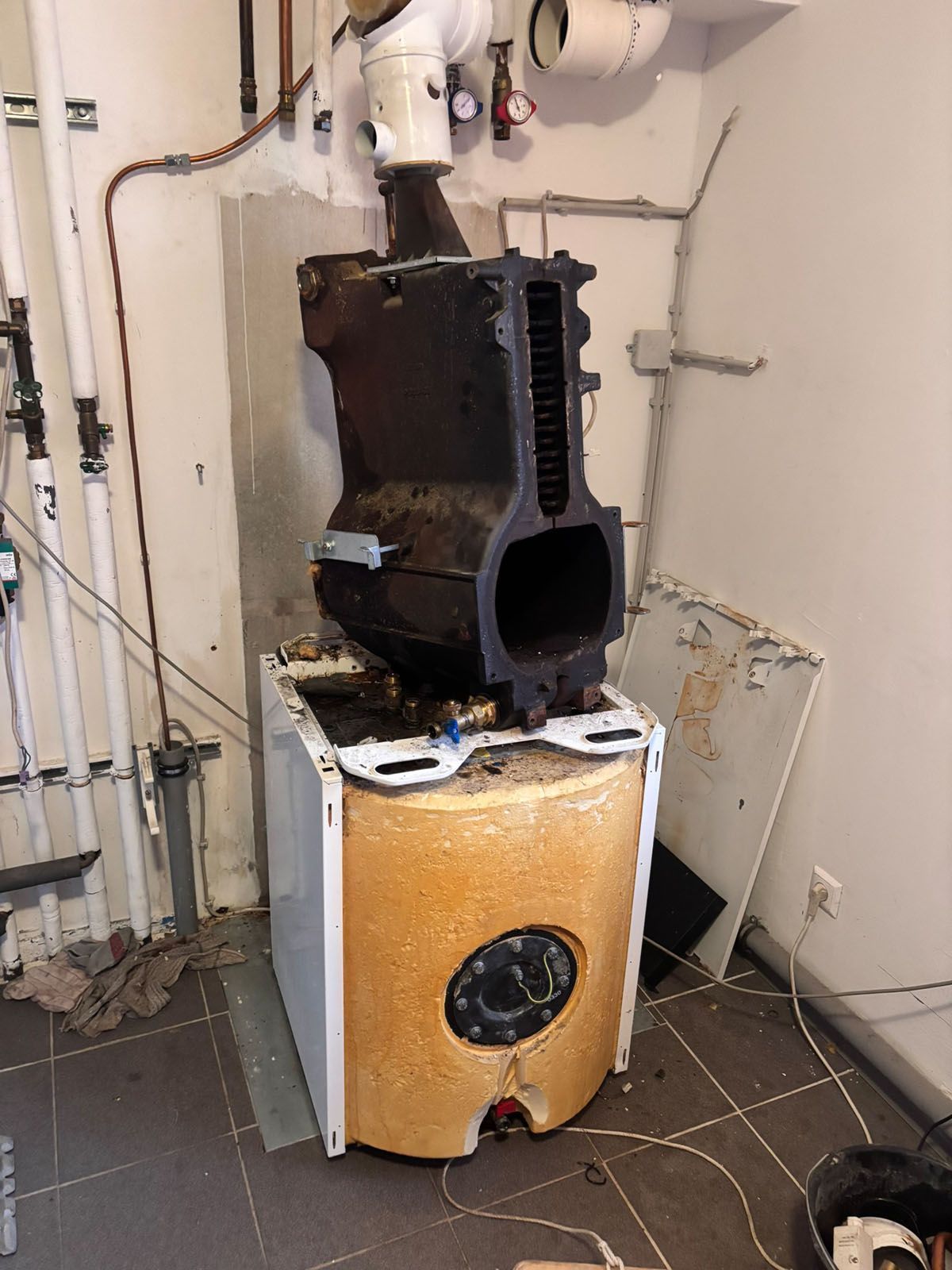 Ein zerlegter Heizkessel in einem Hauswirtschaftsraum, der die Brennkammer, die Isolierung und die Entlüftung zeigt.