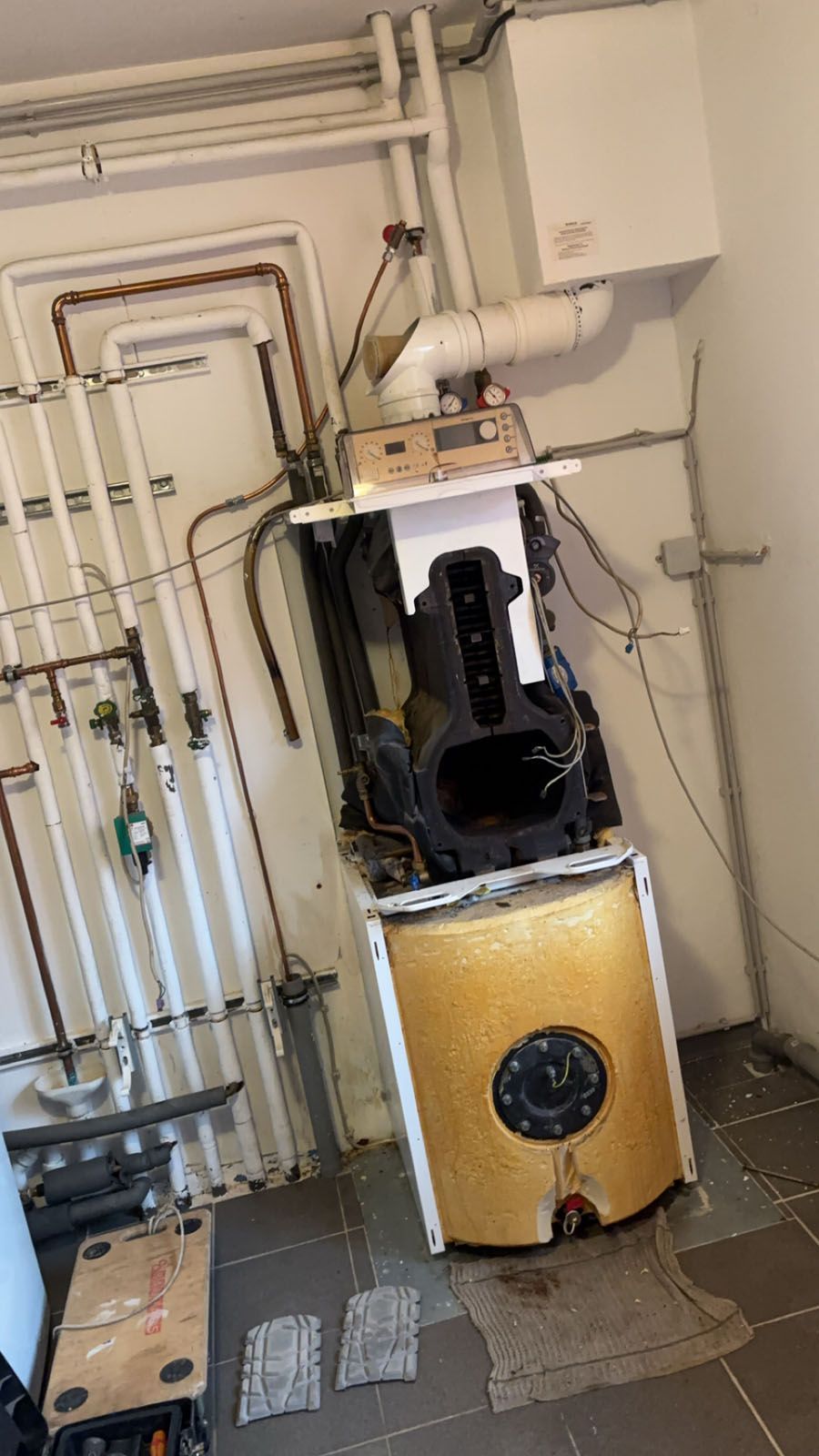 Ein zerlegter Kessel mit freiliegenden Komponenten vor einer Wand mit Rohren.