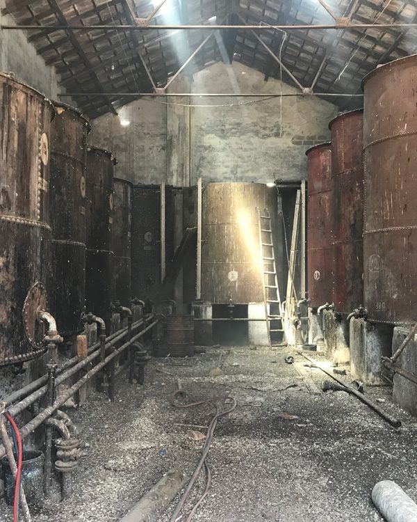 Un almacén lleno de barriles y tuberías oxidadas.