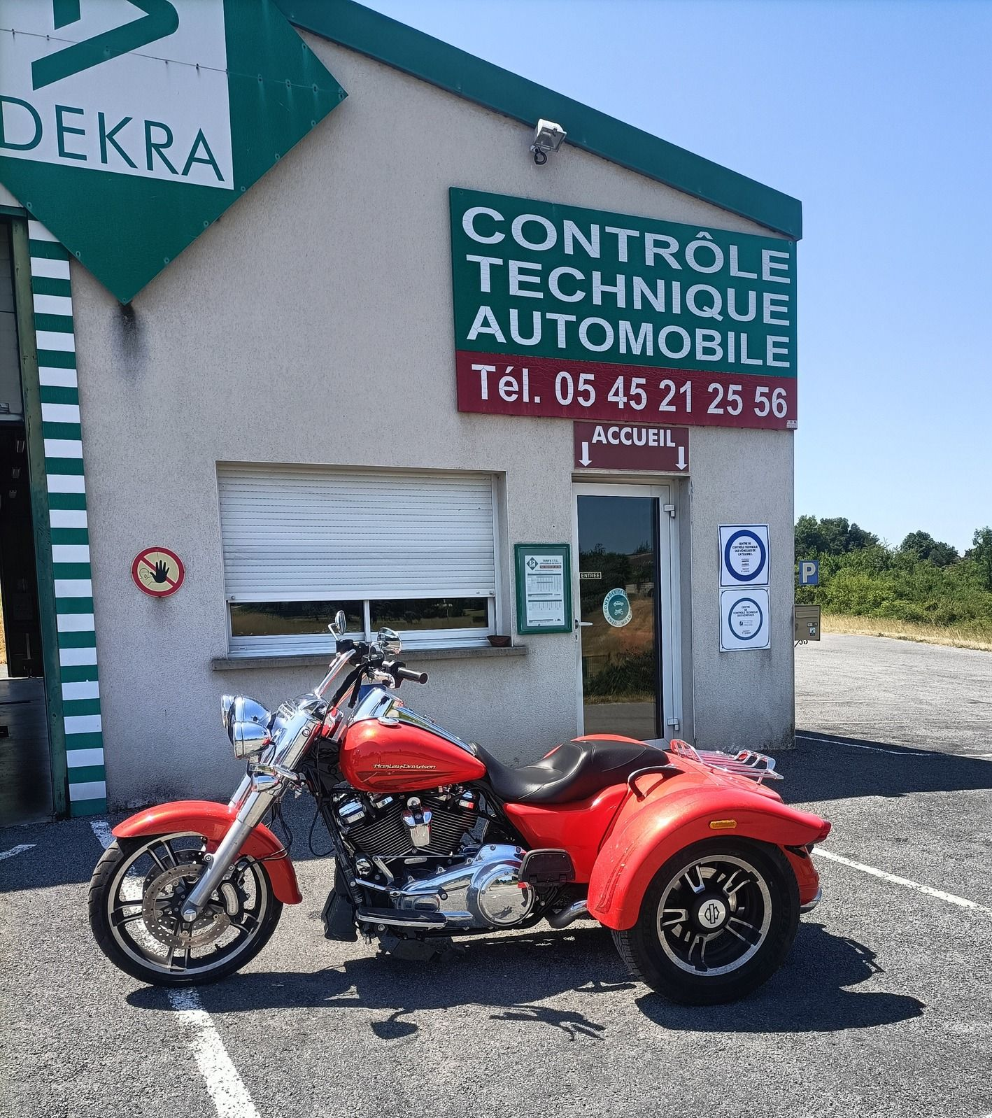 Un trike rouge est garé devant un centre de contrôle technique automobile.