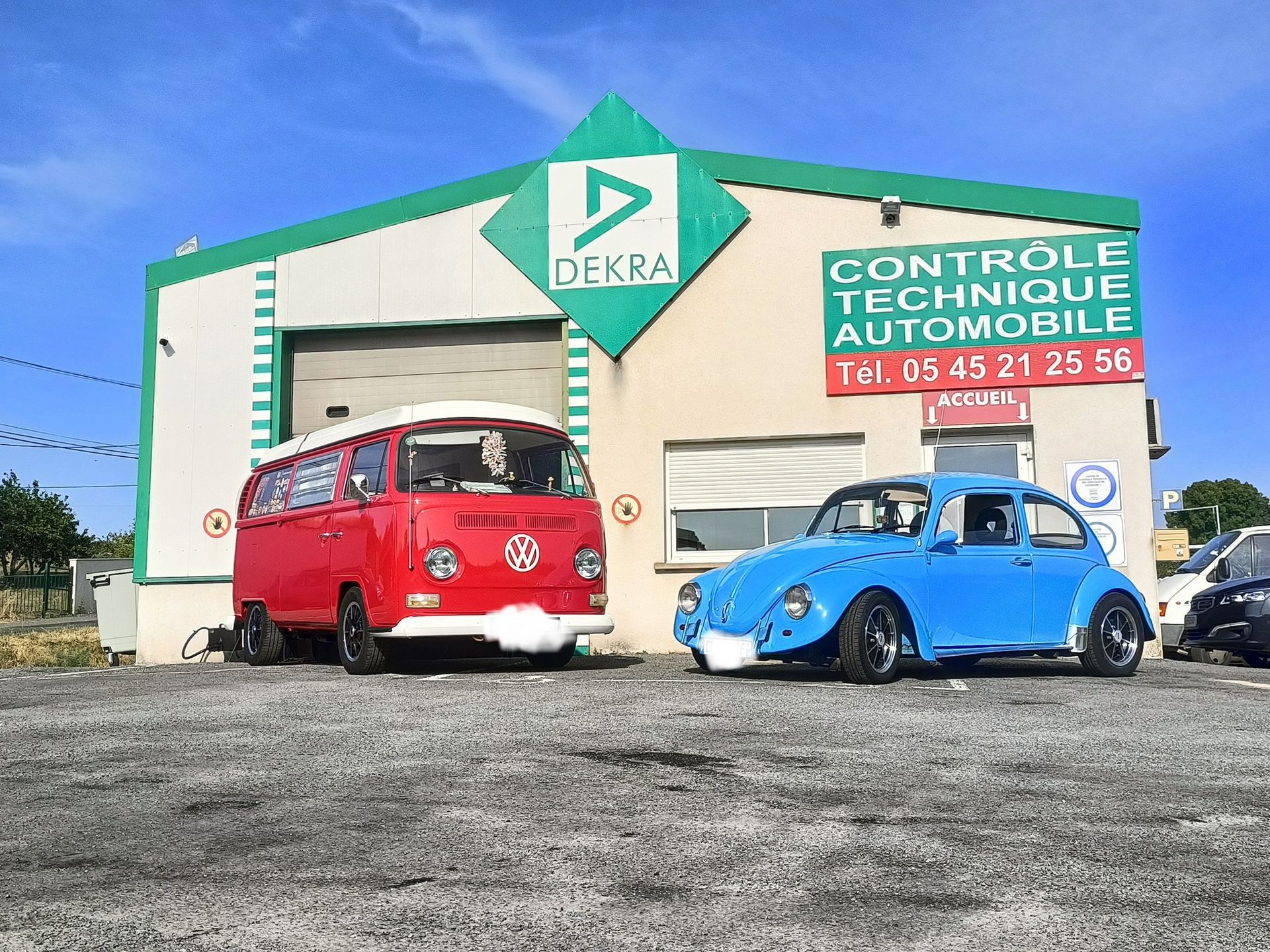 Un combi Volkswagen rouge et une Coccinelle bleue sont garés devant un centre de contrôle technique.