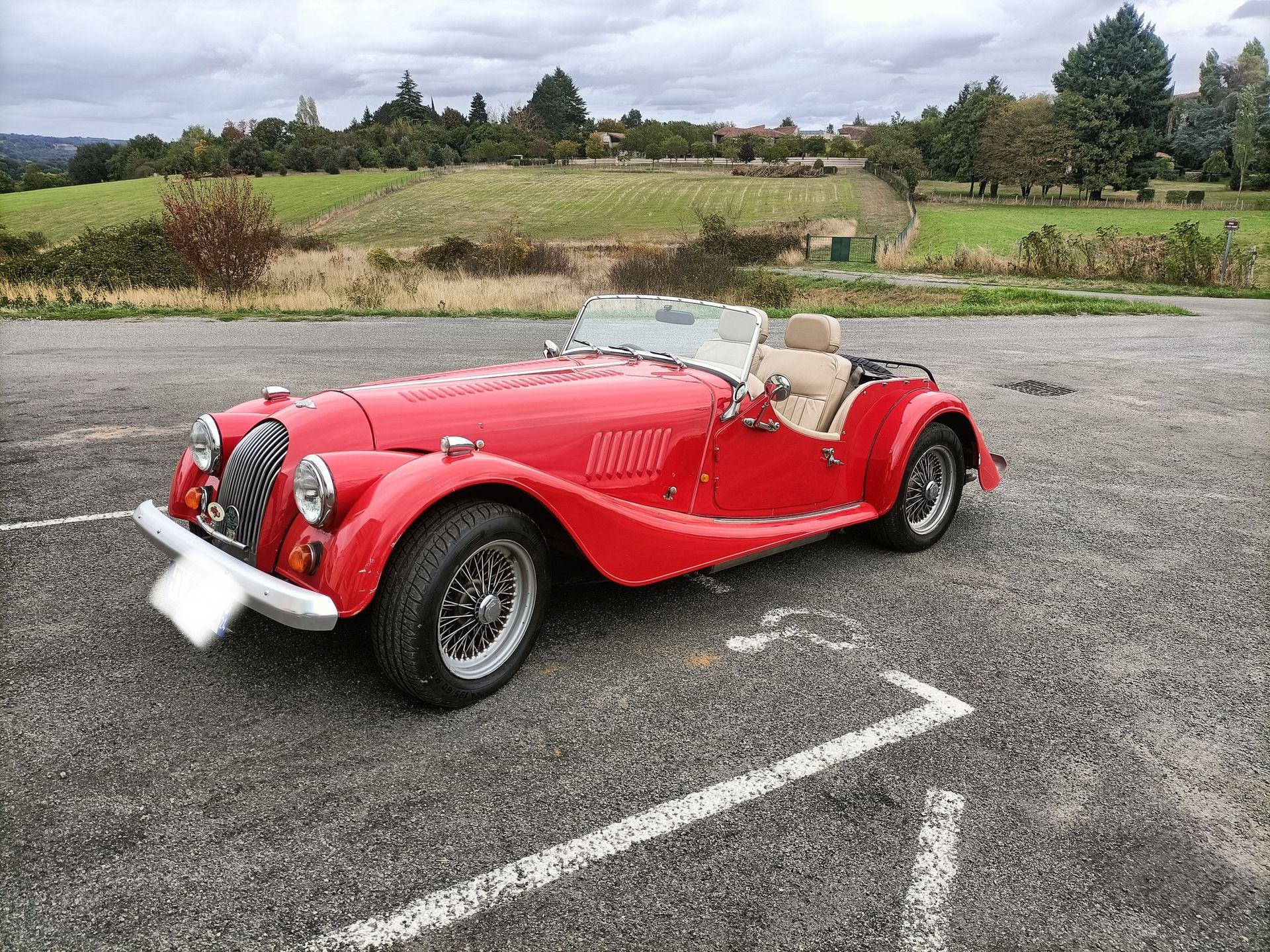 Roadster classique rouge garé sur un parking.