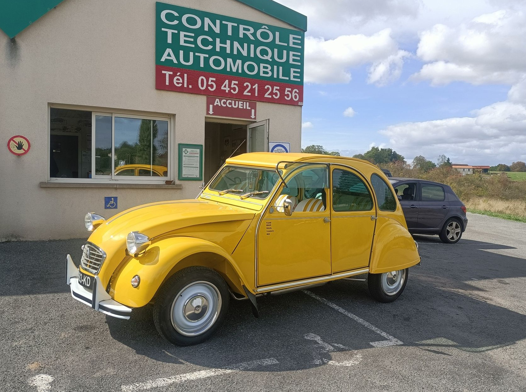 Citroën 2 CV jaune garée devant un centre de contrôle technique.